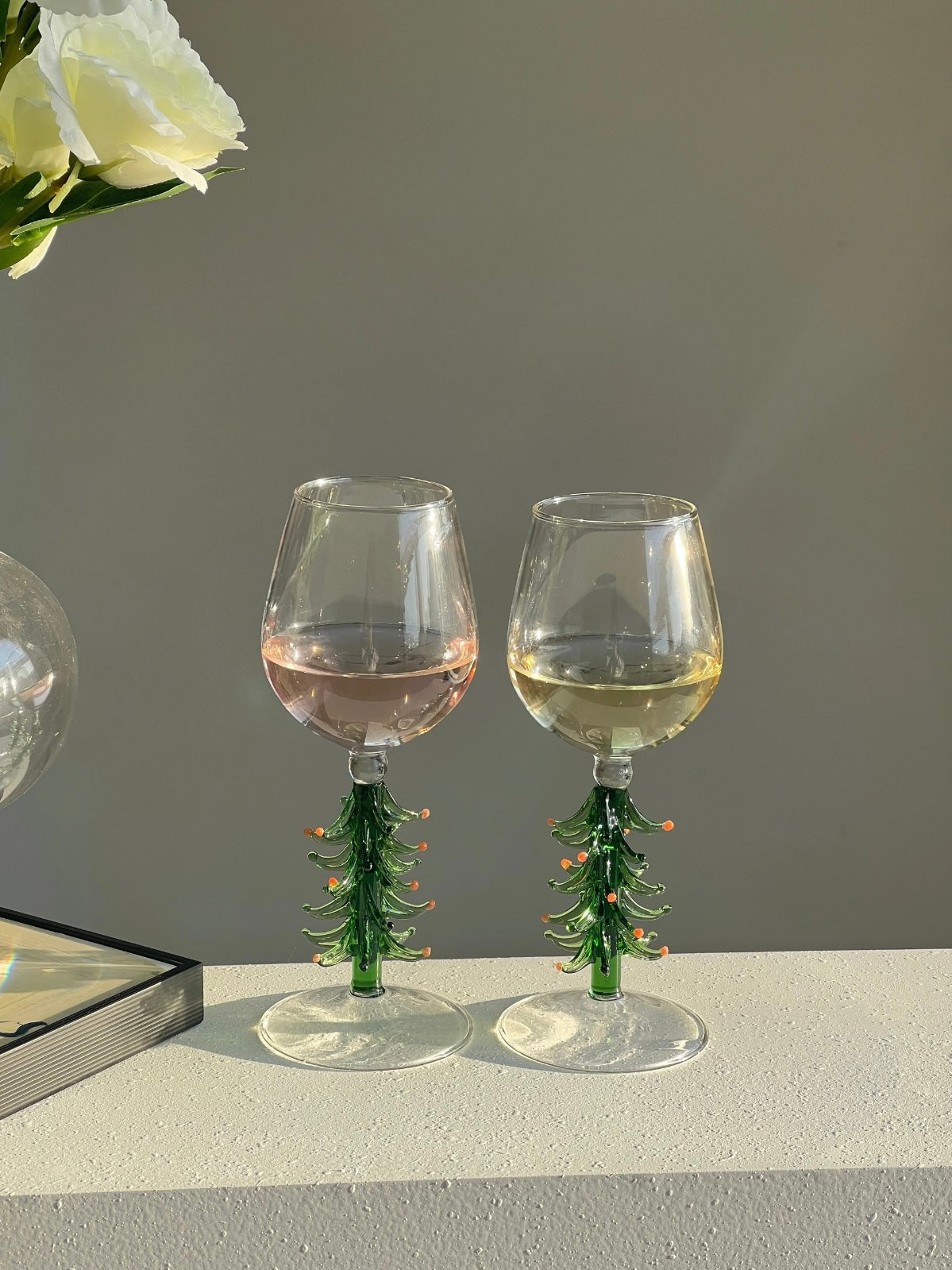 Two Christmas tree wine glasses with green sculptural stems on a light table