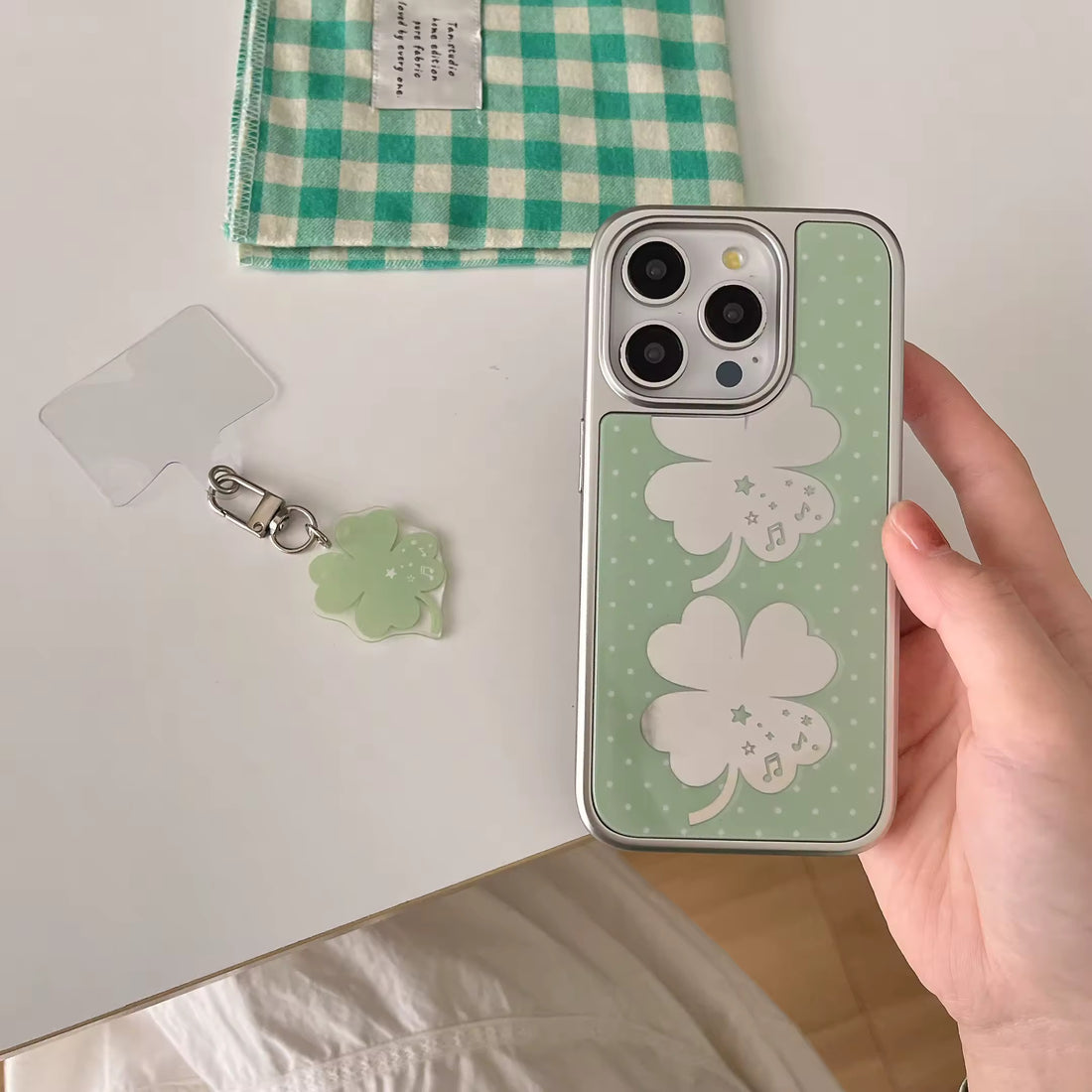 Coquette tech accessory featuring green clover charm and metallic frame iPhone cover