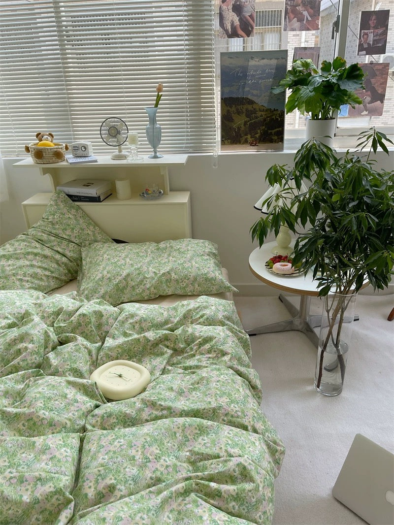 Room with green floral bedding, a plant, and a small table with items.