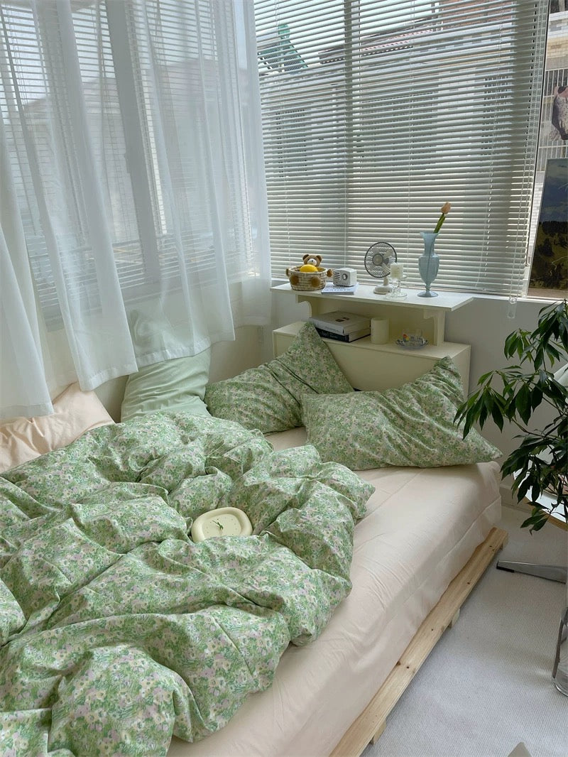 Bed with green floral bedding in a bright room with plants and decor.
