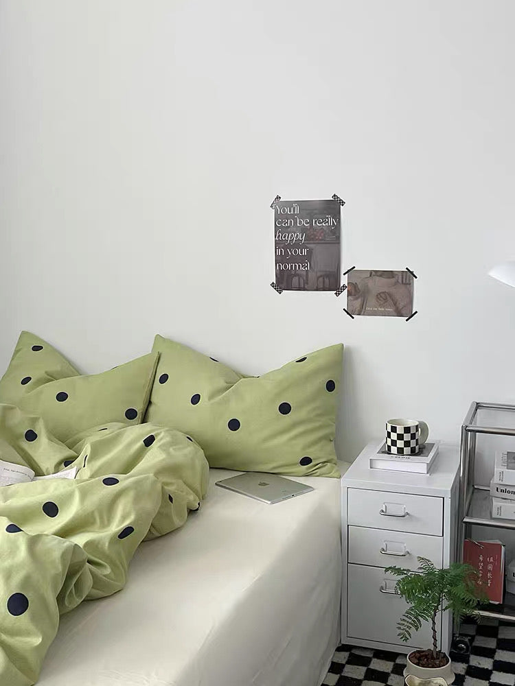 Bed with green polka dot bedding in a room with a white wall and checkered floor.