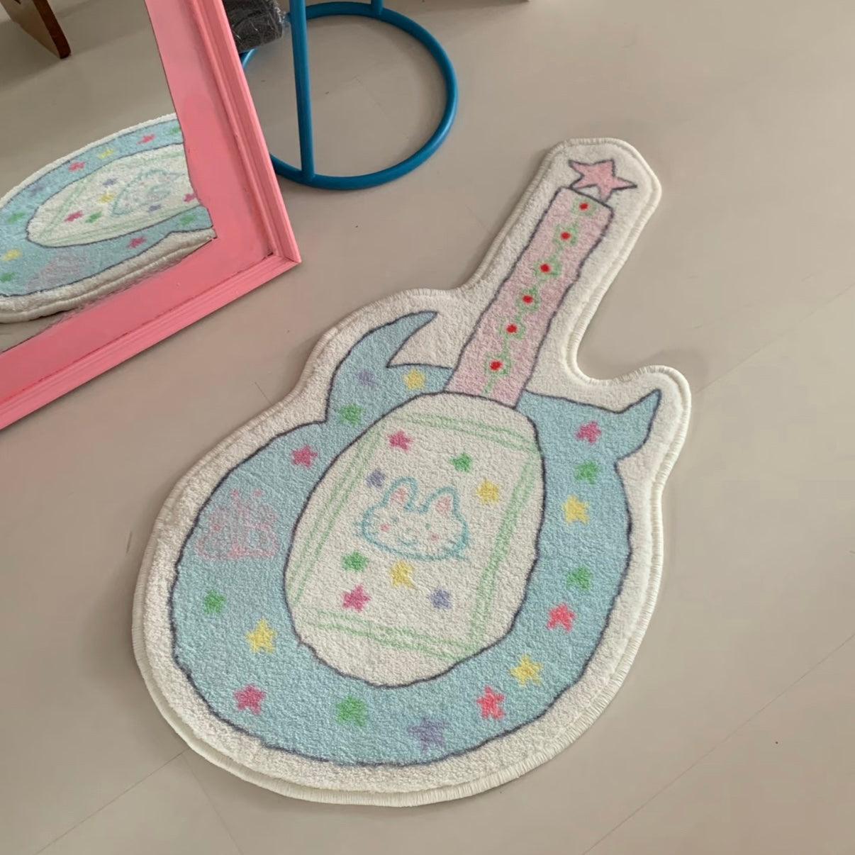 A guitar-shaped plush rug with a pastel bunny design, displayed on a light beige floor next to a pink mirror frame.