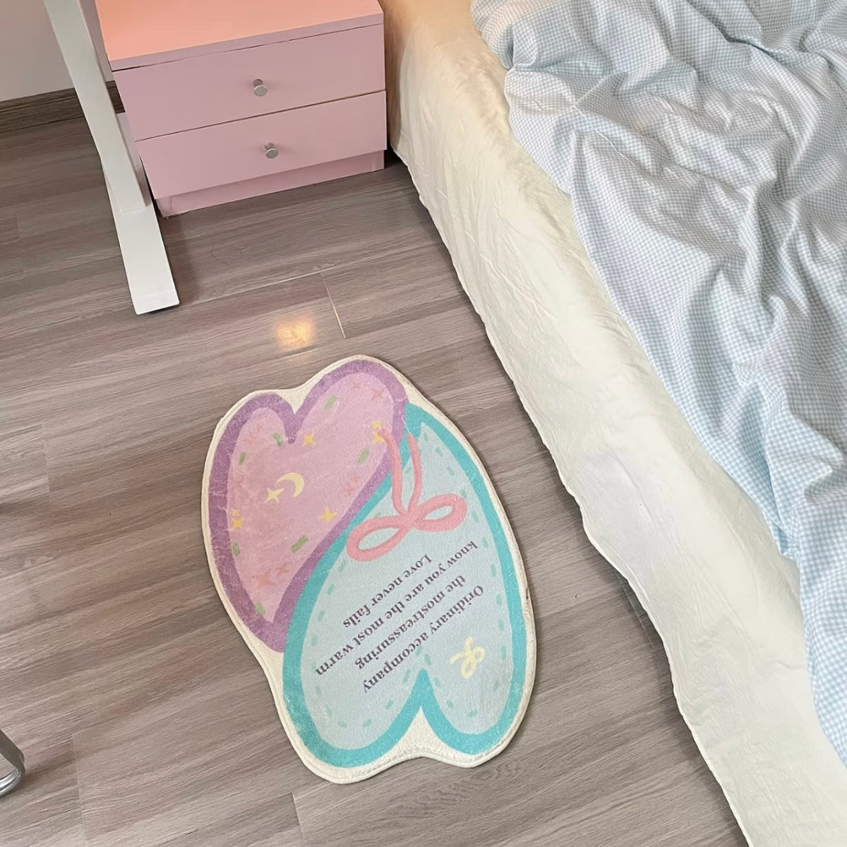 Pastel heart bath mat placed beside a bed with a pink nightstand on wood flooring