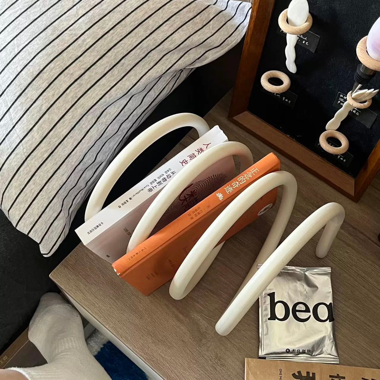 White U-shaped book holder with books on a wooden surface next to a striped blanket.