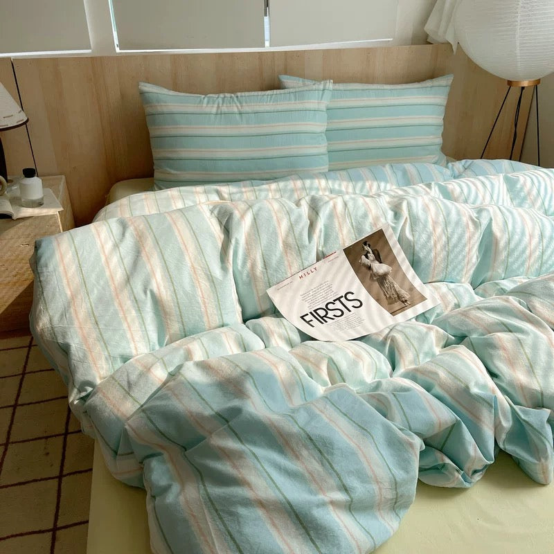 Bed with striped bedding and a magazine on a wooden floor.