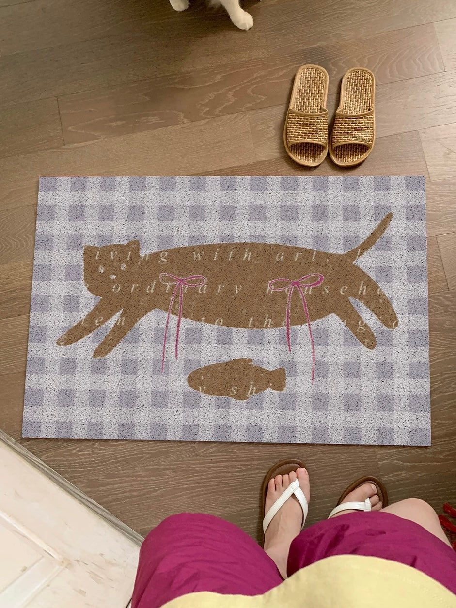 An apple doormat lies at a doorway with two green apples and pink bows over a pale yellow gingham pattern.