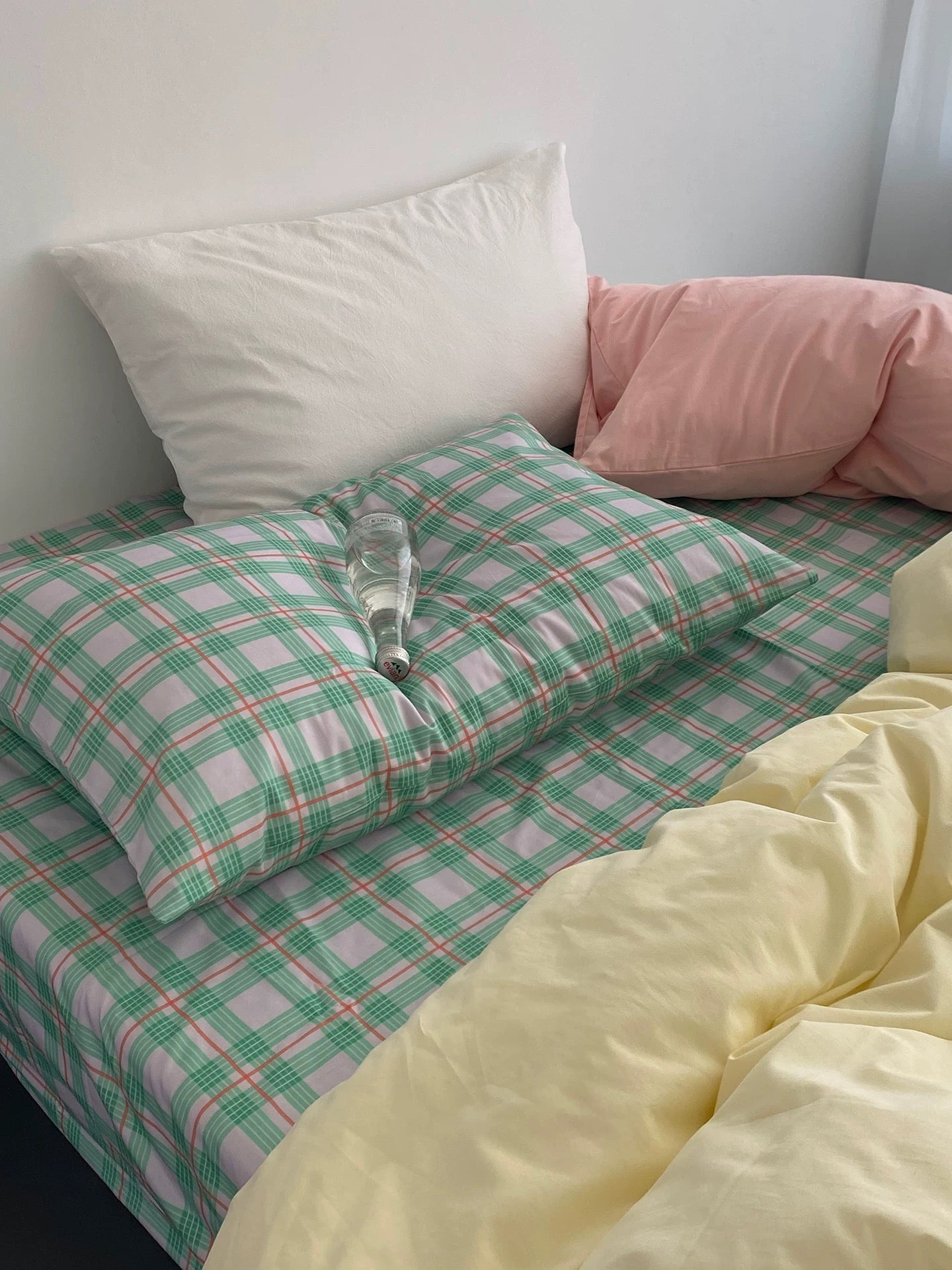 Bed with green and white checkered duvet, pink pillow, and yellow blanket.