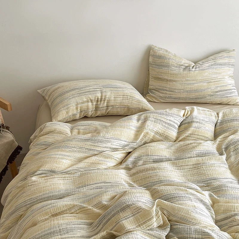 A cozy bed styled with a cream and beige striped duvet cover and matching pillowcases, accented by a solid brown pillow and an open book on the bedside table.
