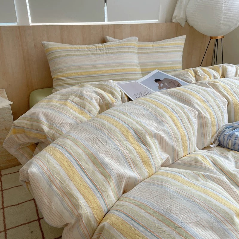 Striped bedding on a bed with a lamp and window in the background