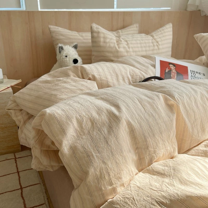 Beige striped bedding on a bed with pillows and a small dog peeking from behind.