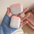 Pink and white checkered air pod cases held by a hand with a blue sleeve.