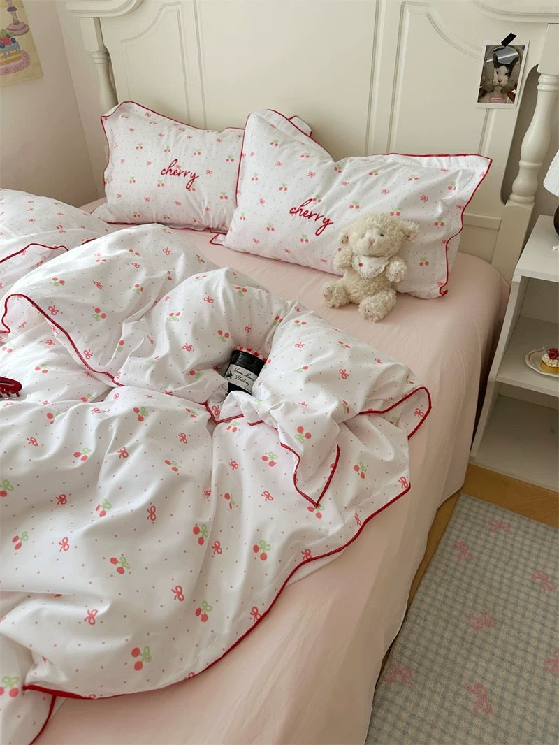 Bedding set with cherry design on a bed with a teddy bear and nightstand.