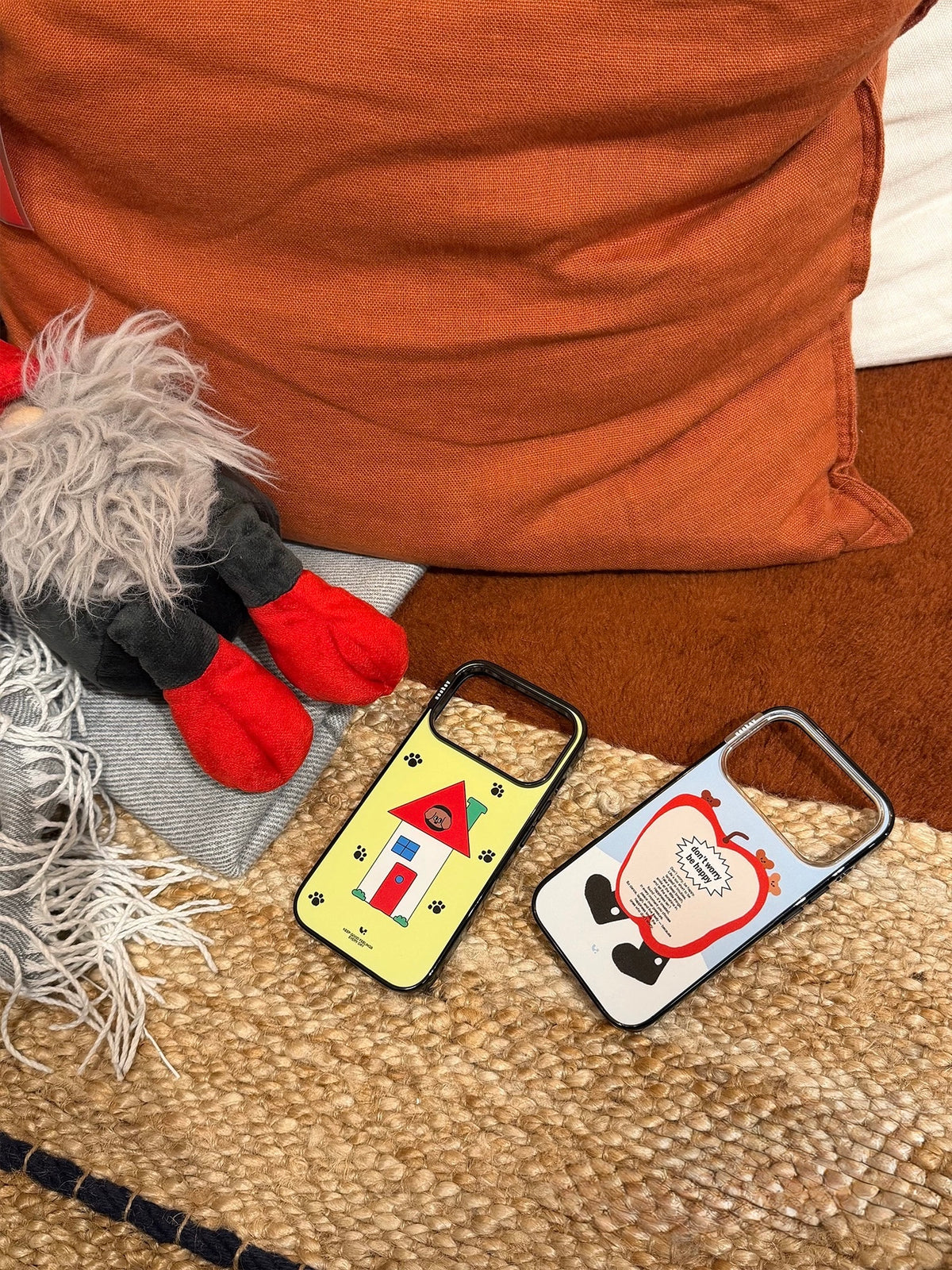 Blue and yellow Kawaii phone case designs lie side by side on a chair, showing apple and dog house artwork.