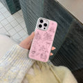 Person holding a pink phone case with illustrations in an outdoor setting