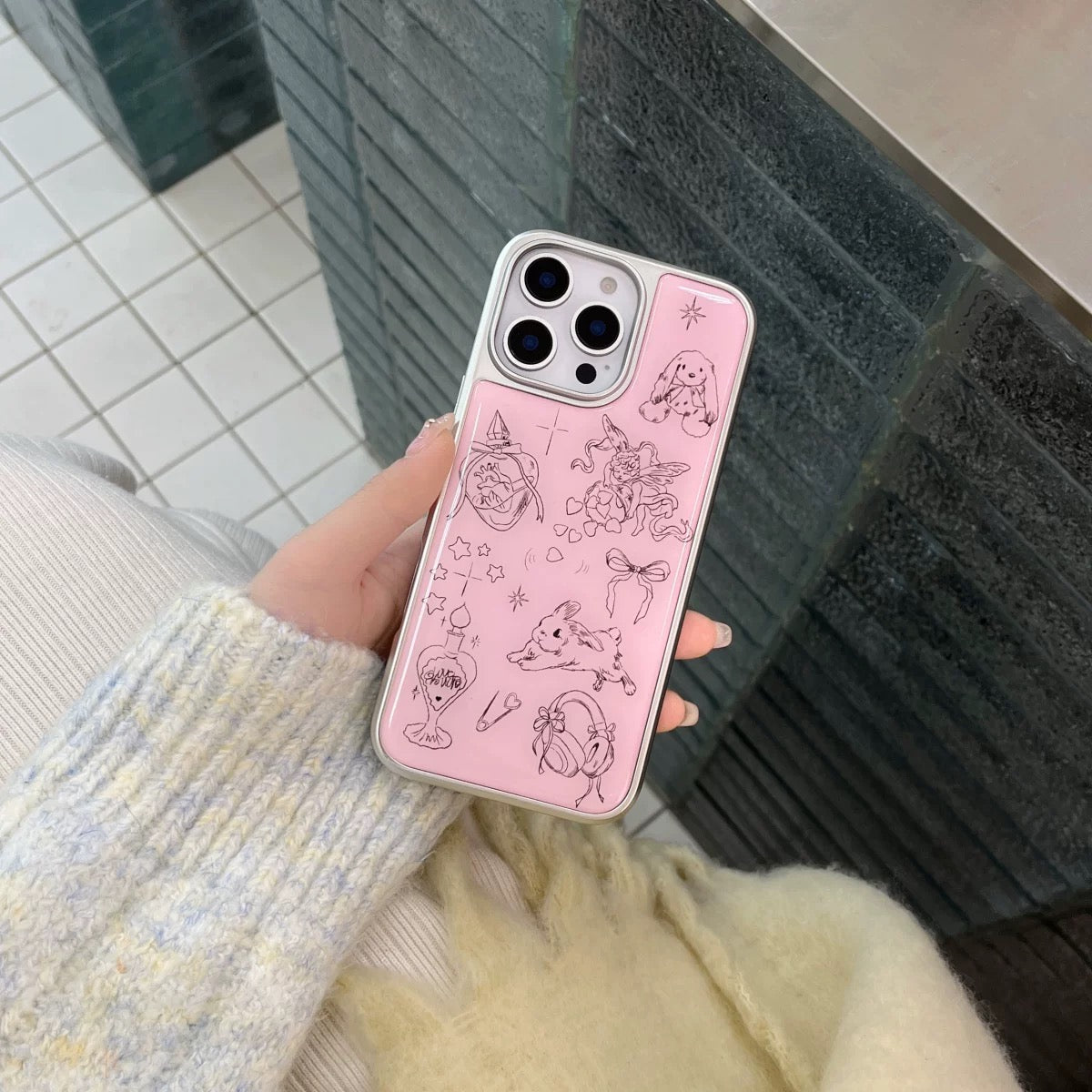 Person holding a pink phone case with illustrations in an outdoor setting