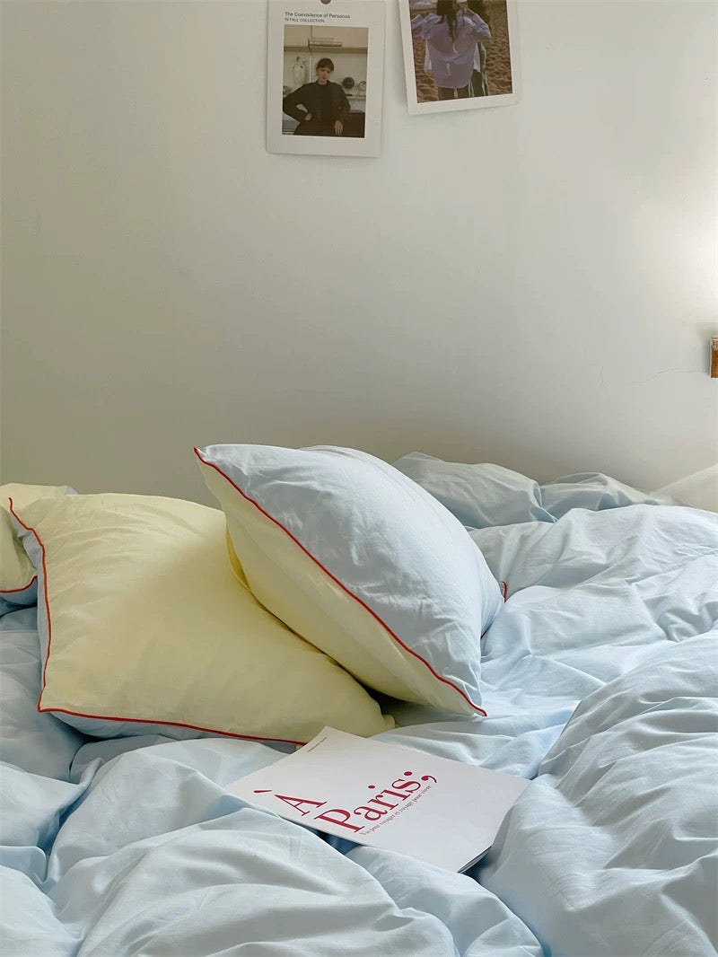 Bed with white and yellow pillows and a 'Paris' book on a light blue comforter.