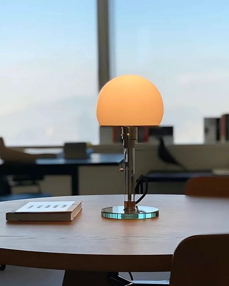 Korean minimalist dome table lamp with glass base and chrome stem glowing beside cream pillows.