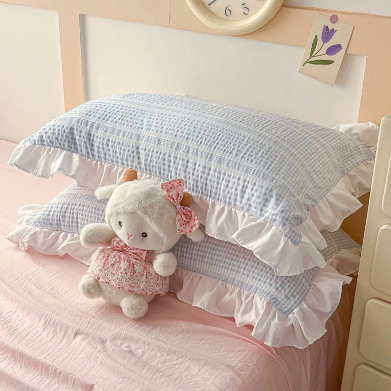 Plush sheep toy on a blue checkered pillow with ruffles on a bed.