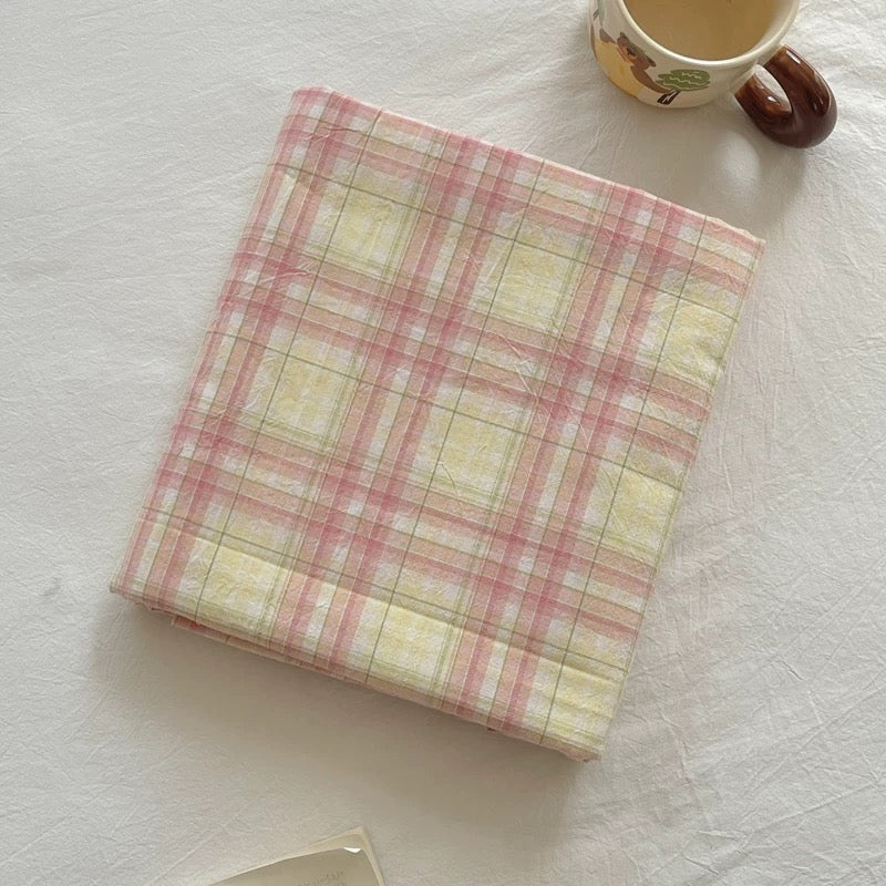 Plaid notebook on a textured white surface with a cup in the corner