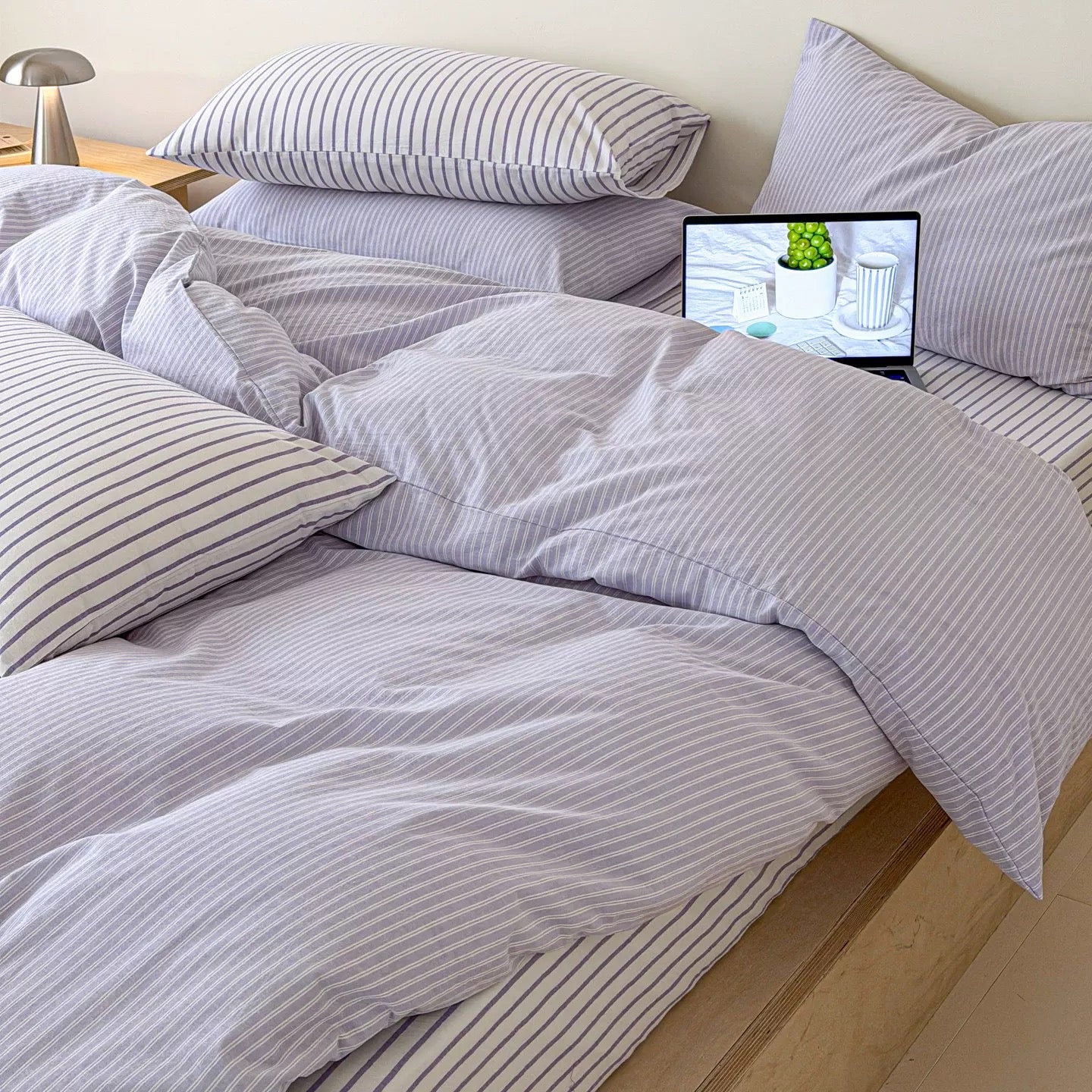 Lavender striped cotton bedding set featuring duvet cover flat sheet and matching pillowcases on minimalist wooden bed