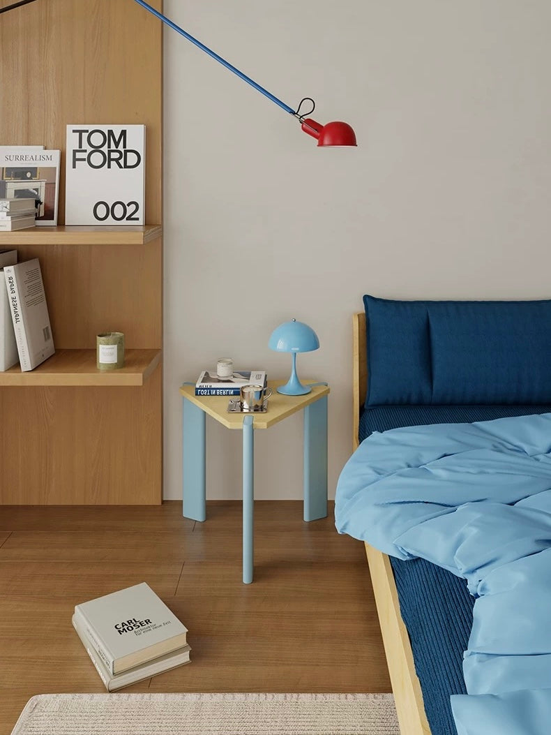 Light blue side table shown closer beside a blue bed, with a dome lamp and small objects on the wood top.