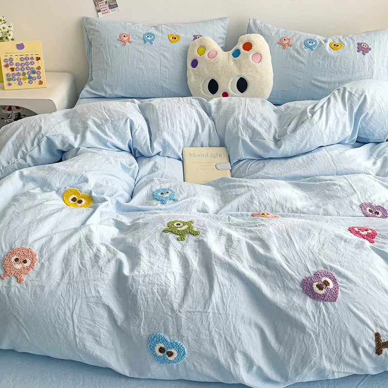 Light blue duvet and pillowcases with colorful cartoon embroidery and a cream character cushion.