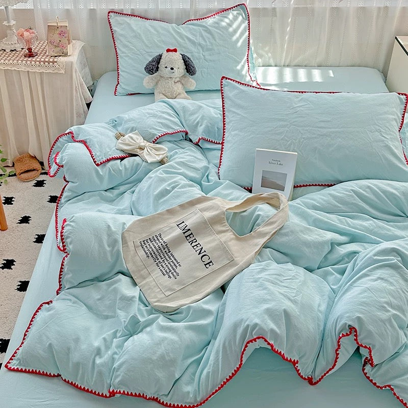 Light blue bedding set with red trim on a bed, featuring a tote bag and plush toy.