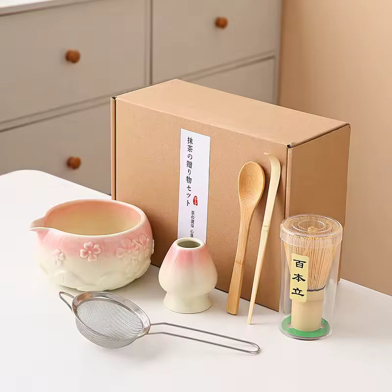 Tea-making set with ceramic bowls, wooden spoons, and a strainer in front of a cardboard box.