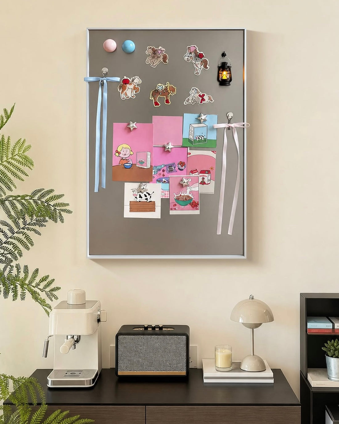 A gray magnetic corkboard with a silver frame, decorated with colorful magnets, stickers, ribbons, and small photos, displayed on a tabletop in a styled home setting.