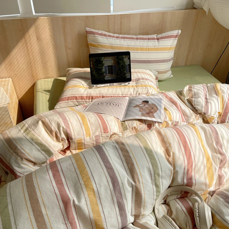 Bed with striped bedding and pillows, featuring a tablet and book on top.