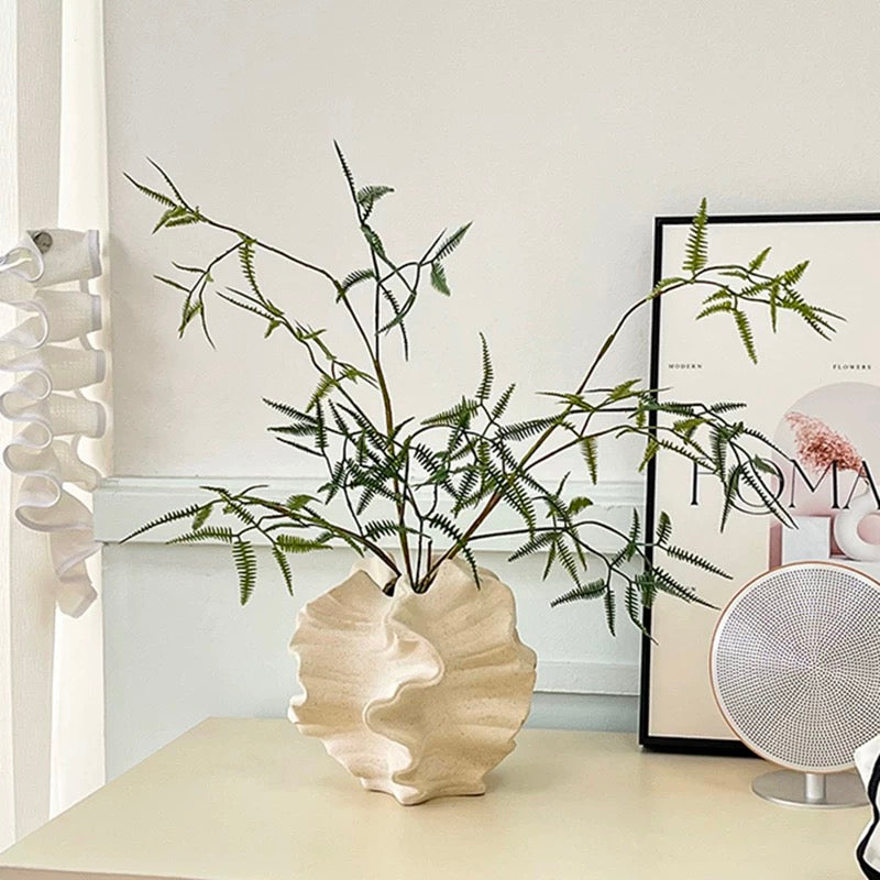 Decorative plant in a white vase on a table with a lamp and books in the background.