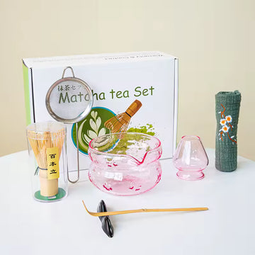 Matcha tea set with various tools and a branded box on a white surface.