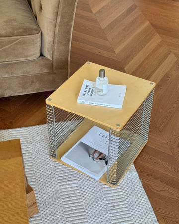 Small square table with a bottle and papers on a wooden floor.