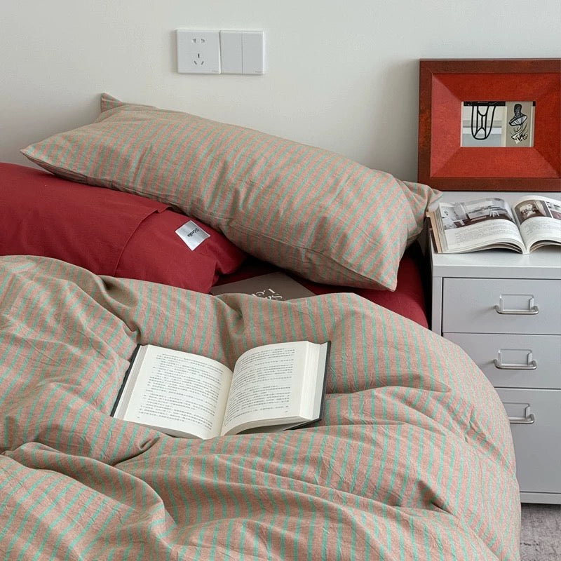 Bed with striped bedding and pillows, open book, nightstand with open book