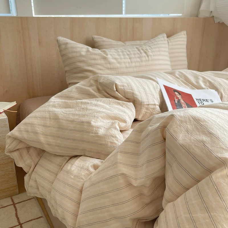 Beige striped bedding on a bed with a magazine on top, in a room with wooden walls.
