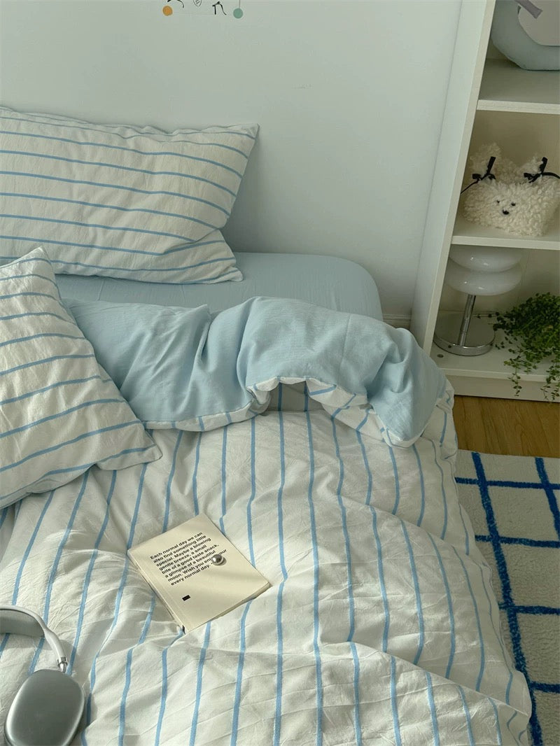 Bed with light blue and white striped bedding in a room with shelves and decor.