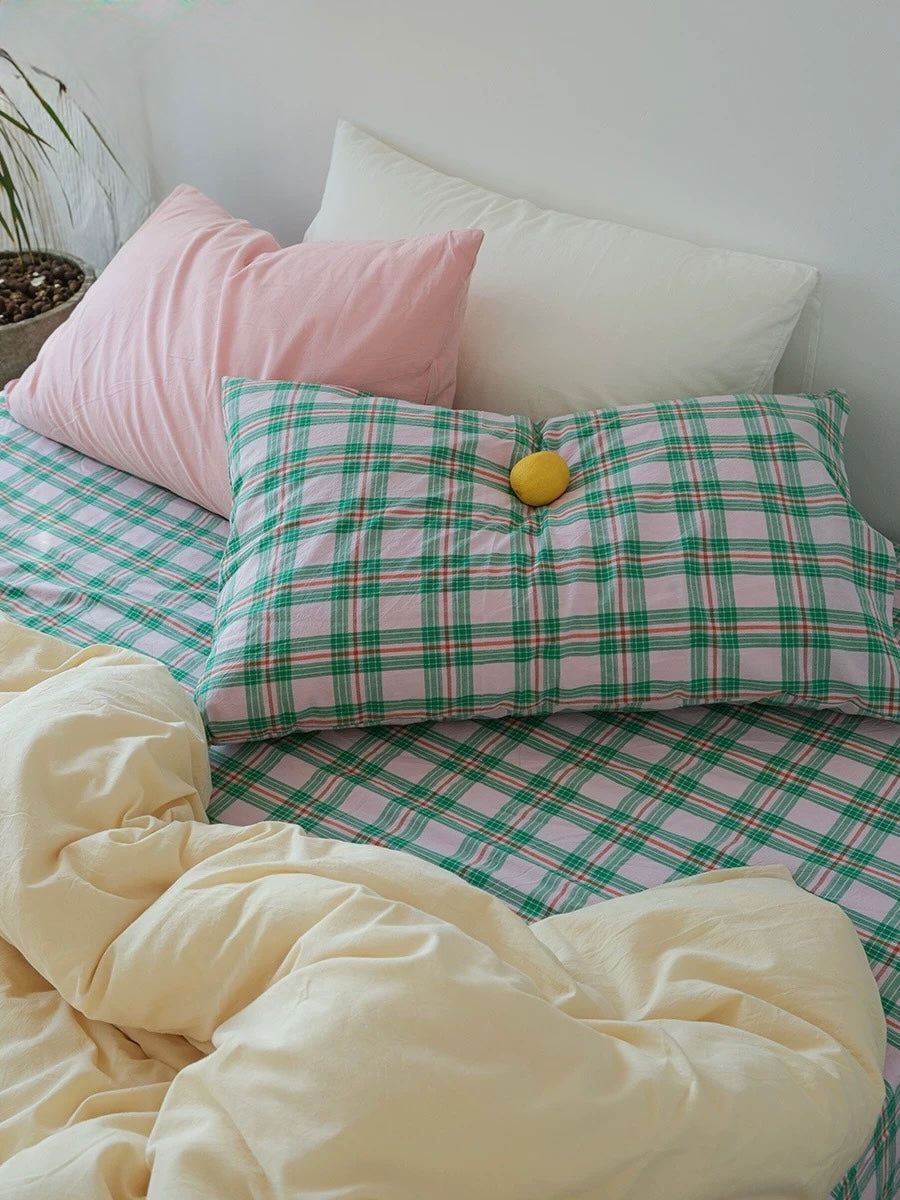 Plaid pillowcase with a yellow ball on a bed with pink and green checkered sheets.