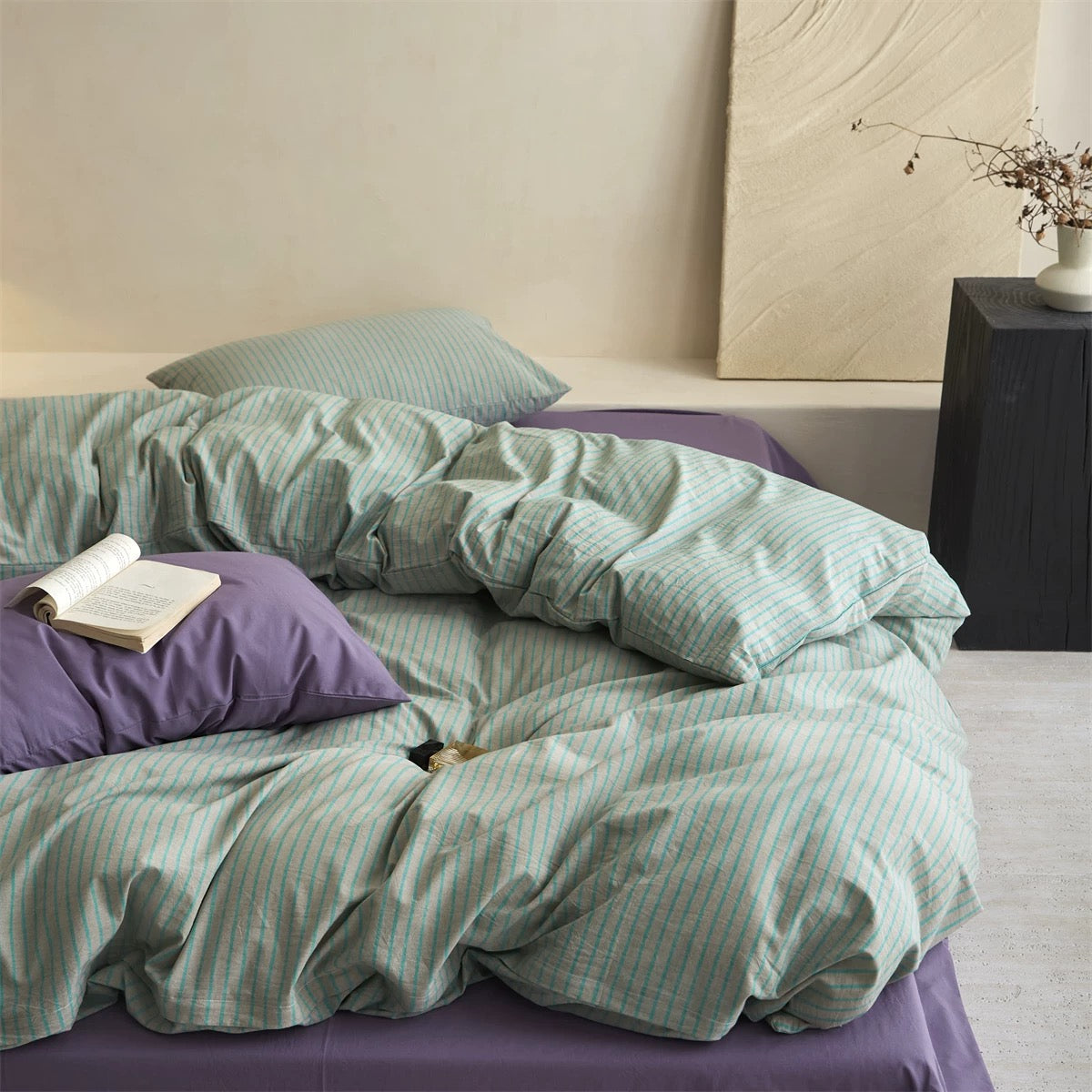 Bed with green striped bedding and purple pillows in a bedroom setting.