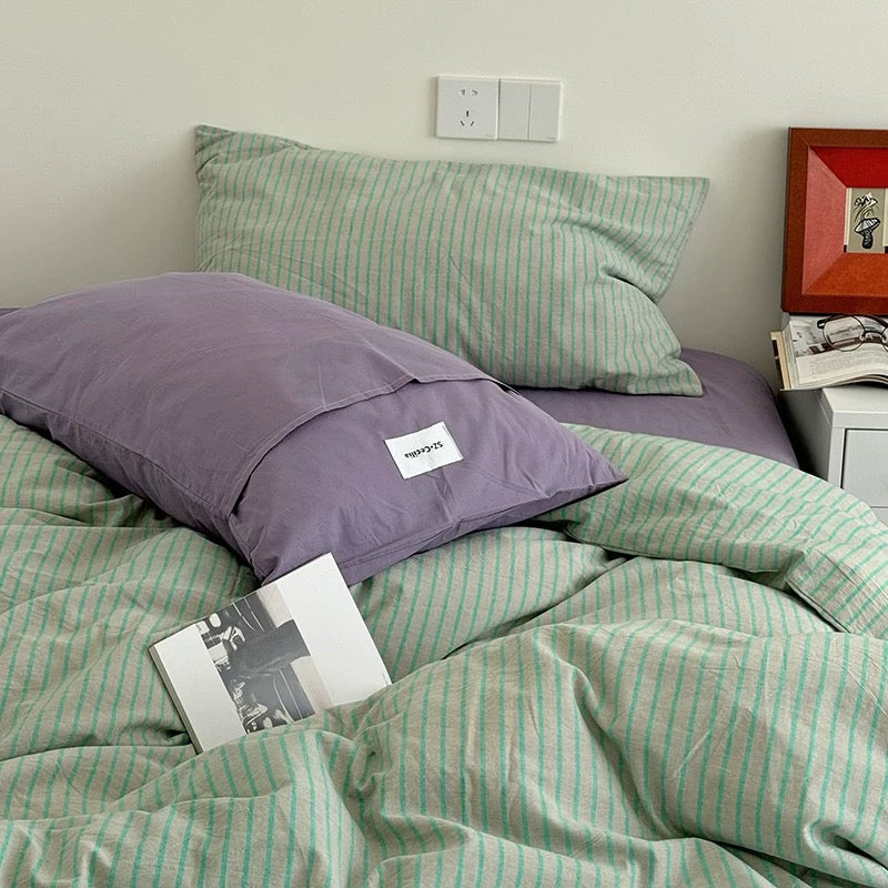 Green striped bedding on a bed with a purple pillow and open book.