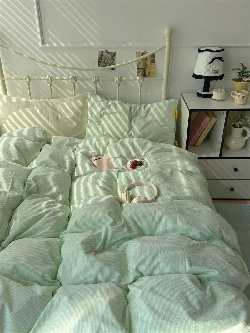 Light green comforter on a bed with a white nightstand and decor items in a bedroom.