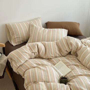 A cozy bed styled with a cream-colored cotton duvet cover and matching pillowcases featuring thin vertical stripes in muted red, orange, and green, accented by solid brown pillows and a brown bed frame.