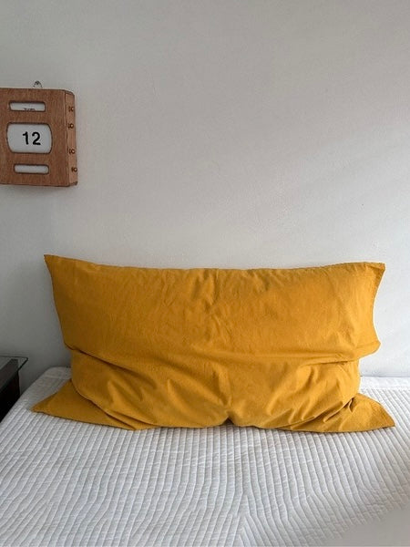 A mustard yellow pillowcase is shown on its own against a white wall.