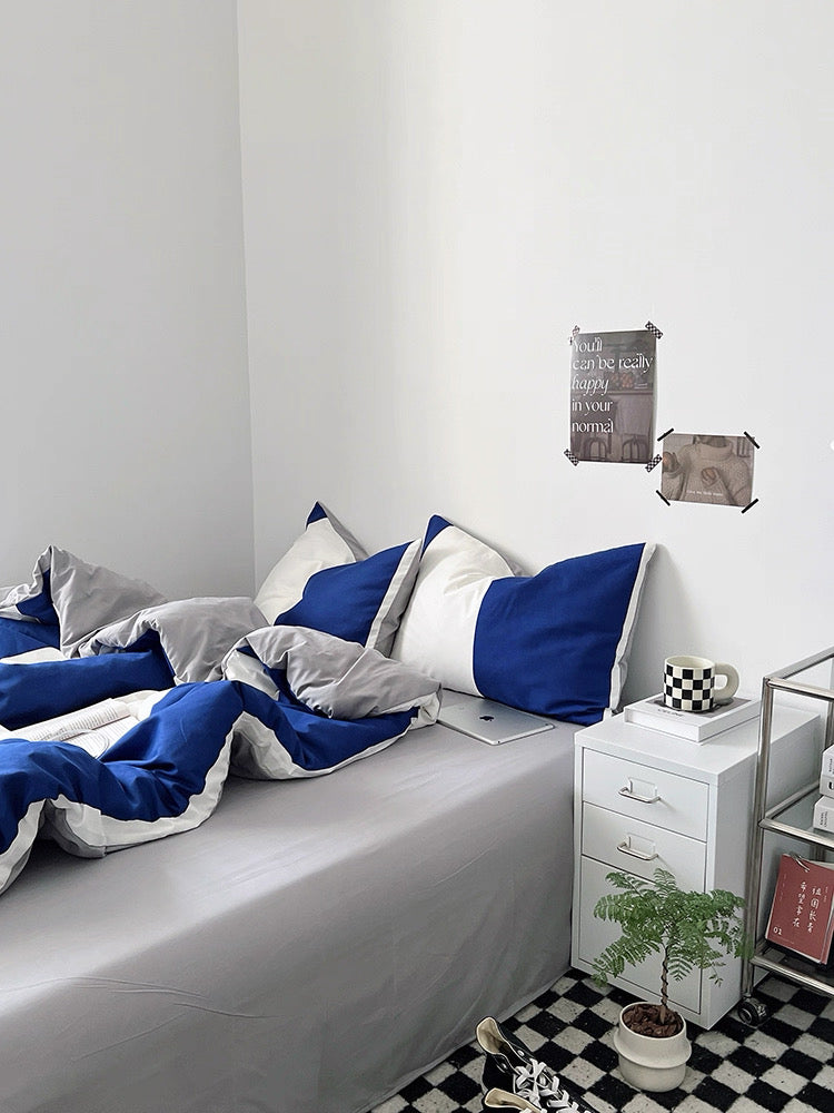 Bedroom with blue and gray bedding on a bed, white nightstand, and decorative items.