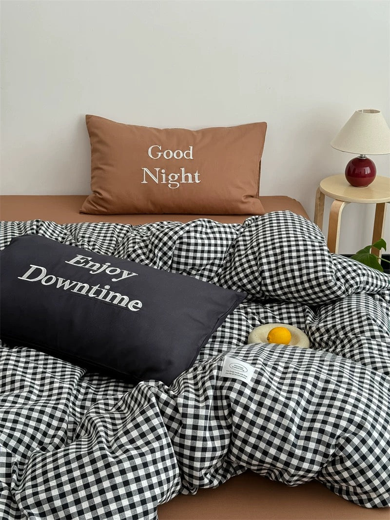 Bed with checkered bedding and pillows with text, side table with lamp in the background