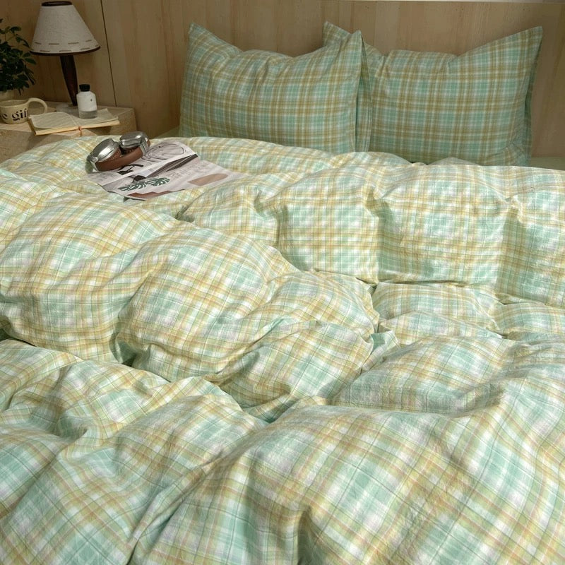 Bed with green and yellow checkered bedding, pillows, and a lamp on a nightstand.