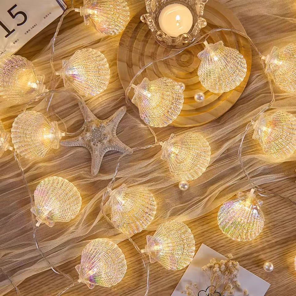 String lights shaped like seashells on a wooden surface with a candle and starfish.