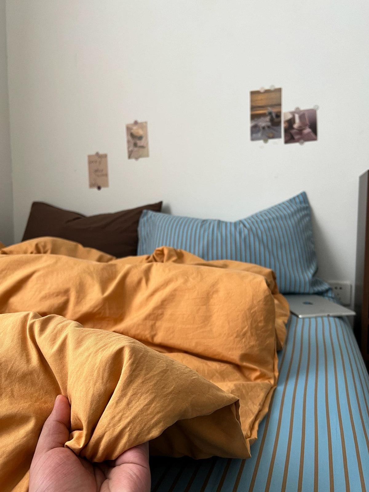 Hand holding the edge of the orange duvet cover above the blue striped flat sheet