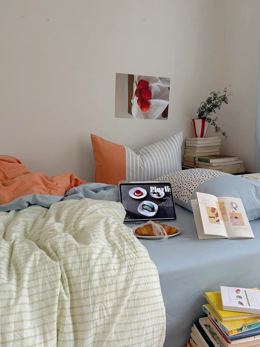 Pastel bedding is pulled back to show a blue sheet, a tablet, an open book and peach-panel pillows.