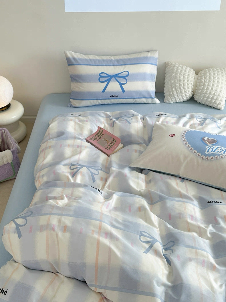 Bed with blue and white checkered bedding, decorative pillows, and a small plant on a nightstand.