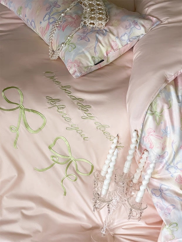 Pink satin fabric with green embroidered text and decorative elements on a bed.
